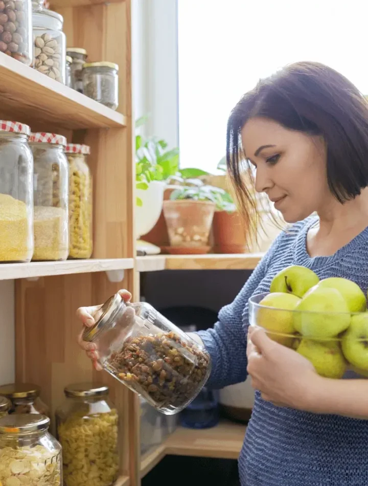 Mulher olhando um pote de grãos segurando uma bacia de maçãs